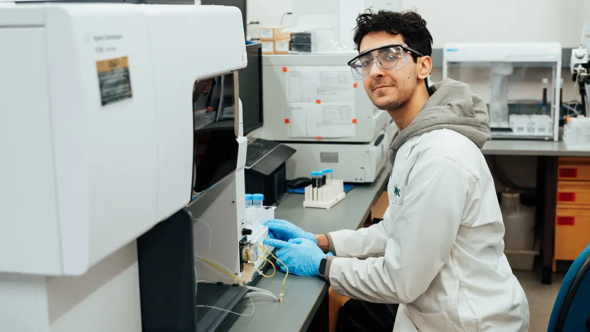 Ahmad Jalil, wearing safety glasses, a lab coat, and blue gloves, works with scientific equipment at a workstation in UNBC’s NALS Matter Lab.